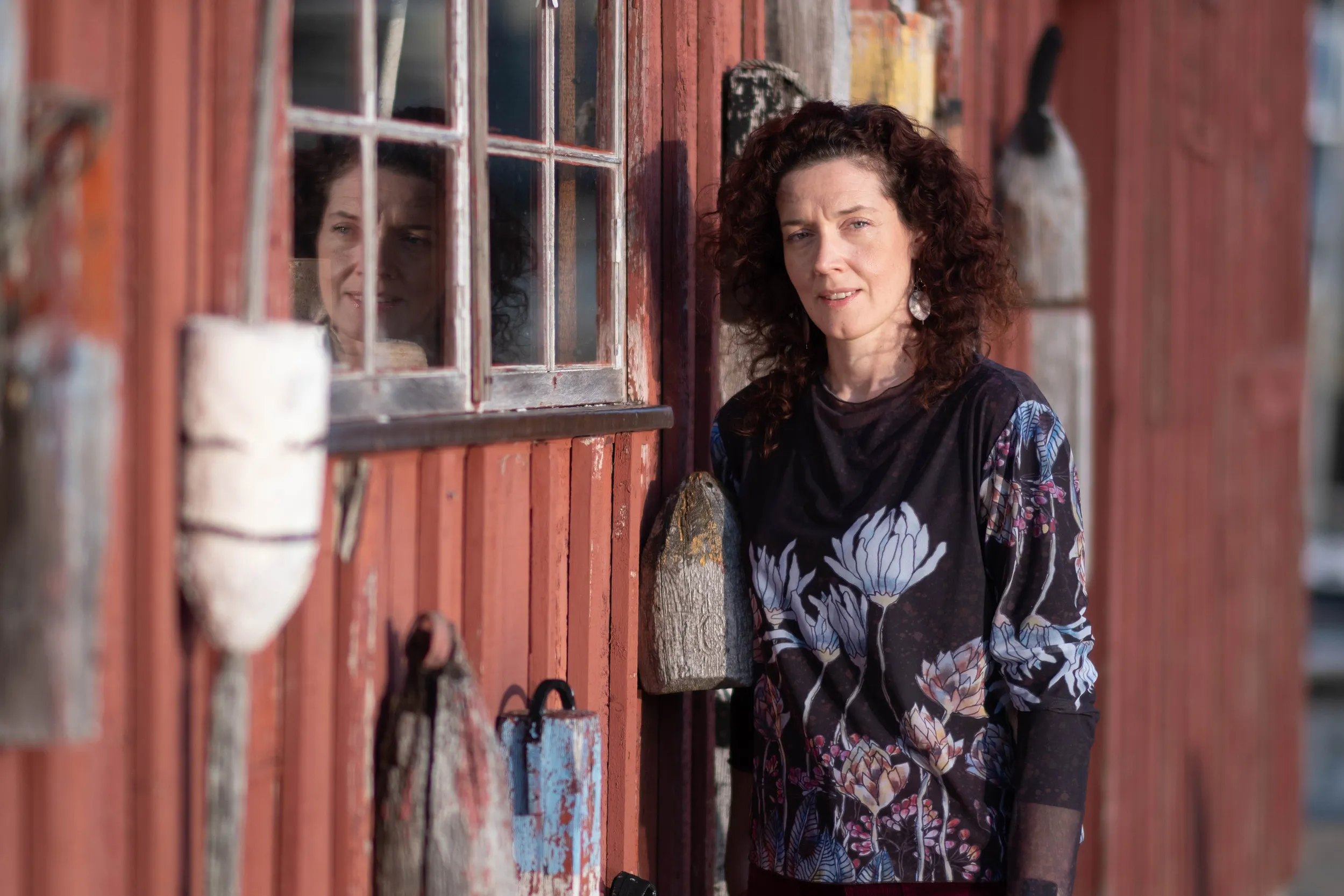 Woman in a floral top standing beside a red fishing shack