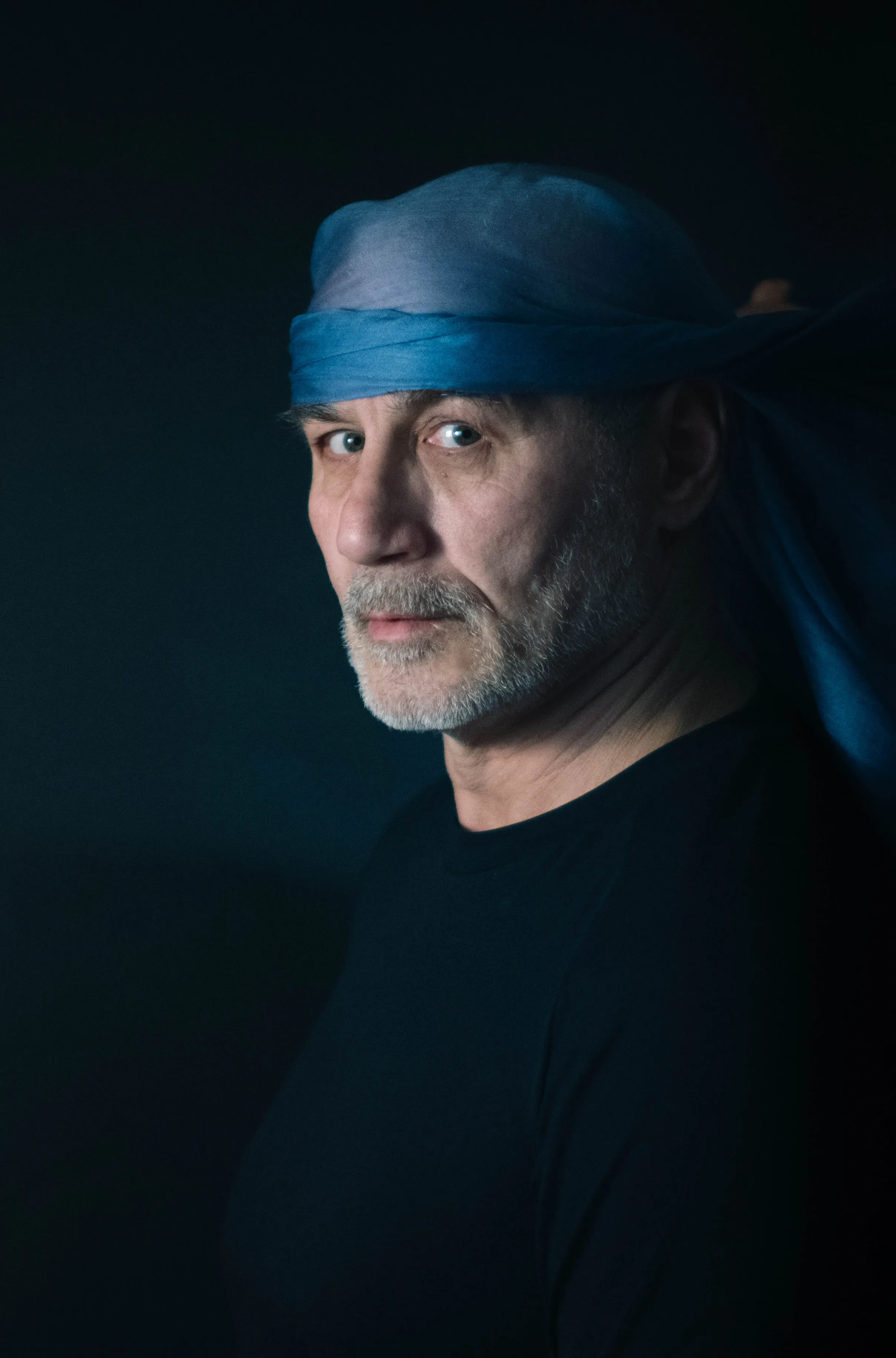 Close portrait of a man in a blue headscarf against a dark background