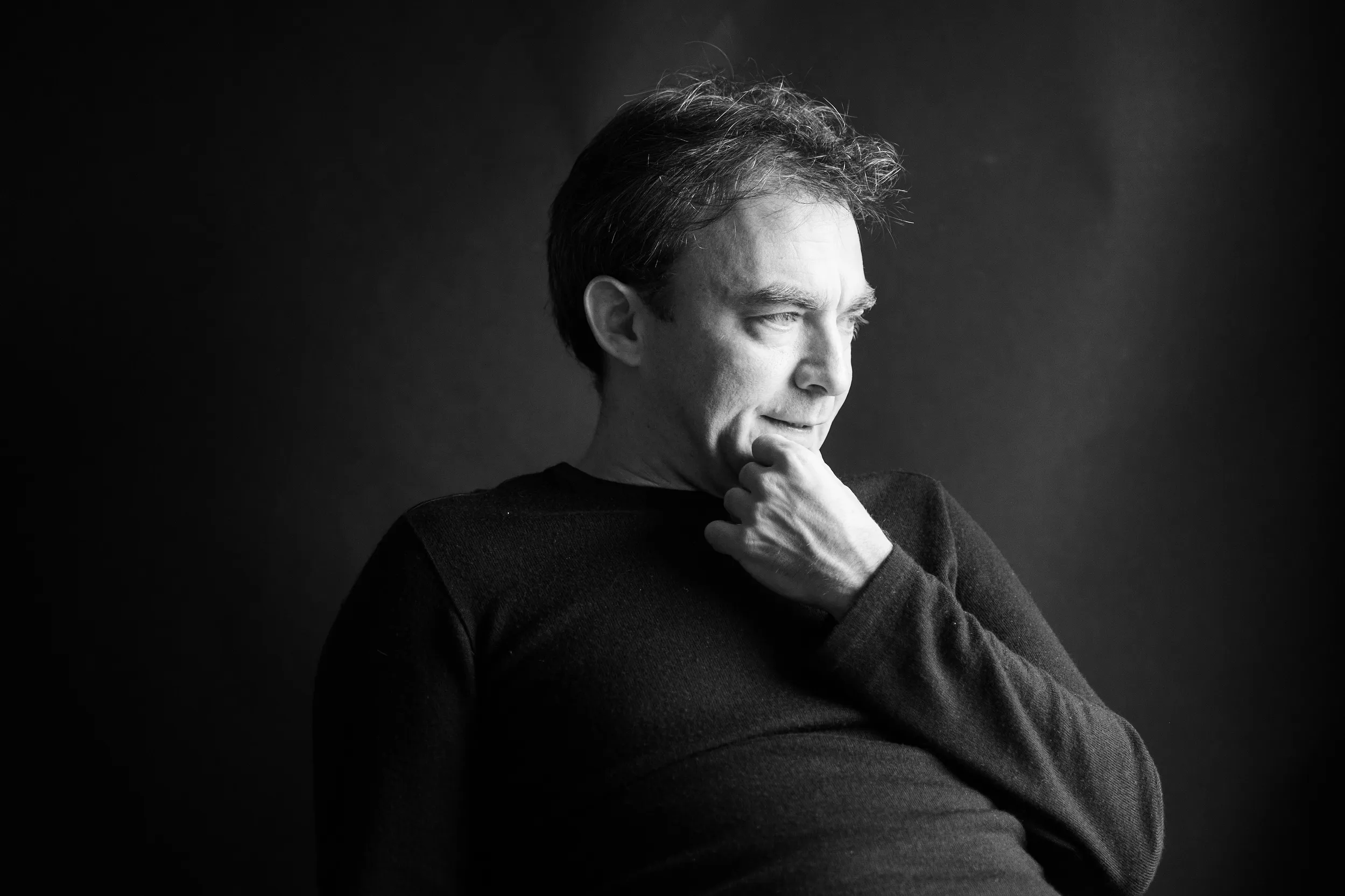 Black-and-white studio portrait of a man, hand at his chin