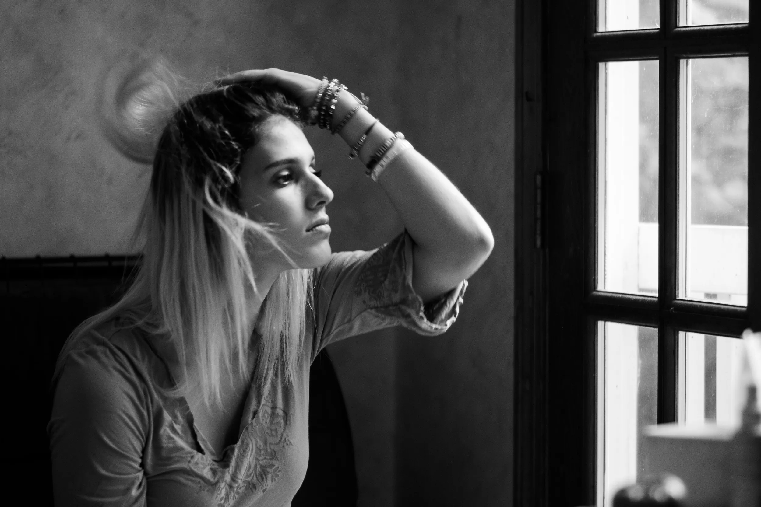 Black-and-white portrait of a woman by a window, hand in her hair