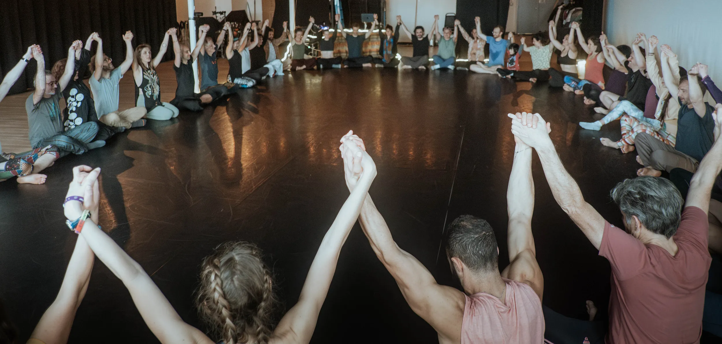 Dancers seated in a circle, hands joined and raised